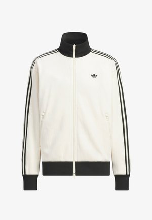 Valkoinen vetoketjullinen treenitakki, jossa musta kaulus, hihansuut ja helma; mustat kolmen raidan yksityiskohdat hihoissa; pieni musta Adidas-trefoil-logo rinnassa.