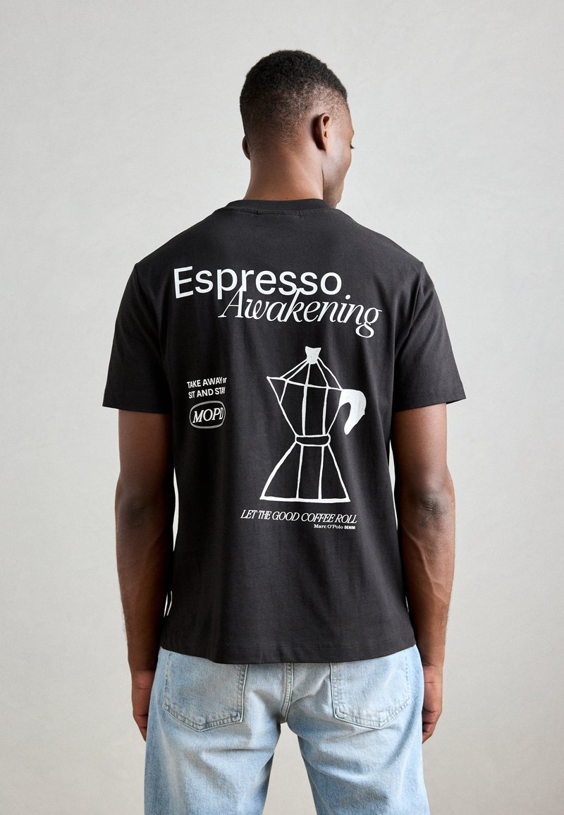 Black cotton t-shirt featuring white text and a graphic of a coffee maker. Cut with short sleeves and a relaxed fit.