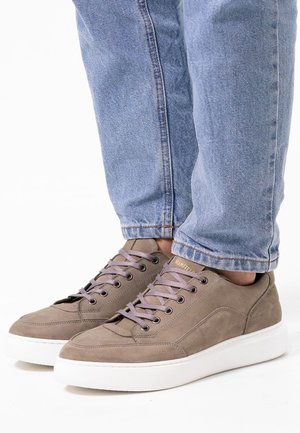 Gray suede sneakers with light purple laces, white rubber soles, and subtle stitching details, paired with light blue jeans.