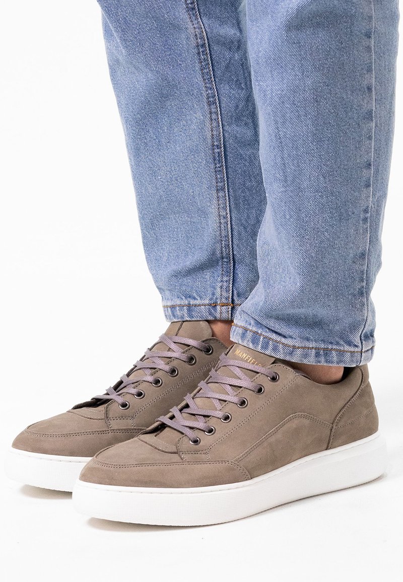 Graue Wildledersneaker mit helllila Schnürsenkeln, weißen Gummisohlen und dezenten Nähdetails, kombiniert mit hellblauen Jeans.
