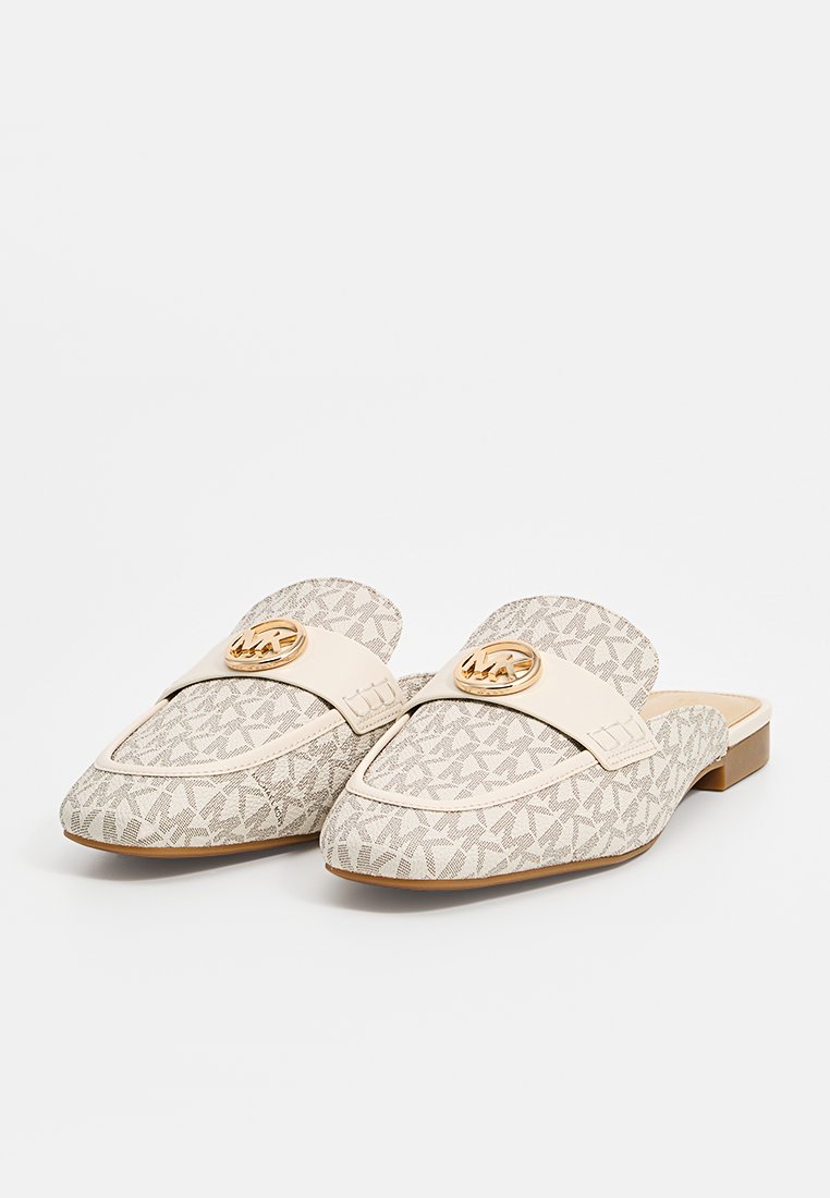 Beige instappers van een gestructureerde stof met een logo patroon, een contrasterende band en een opvallend logo hardware detail aan de voorkant.