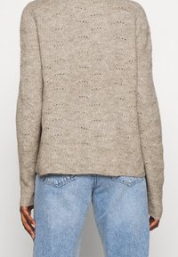 Maglione beige lavorato a maglia con una vestibilità ampia, caratterizzato da un motivo testurizzato e maniche lunghe, abbinato a jeans in denim azzurro chiaro.