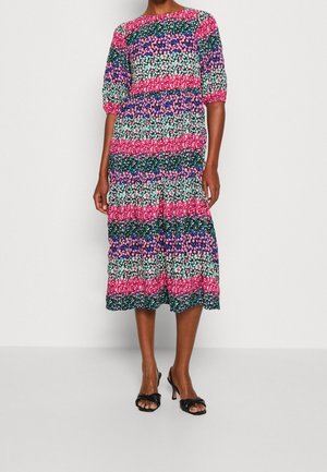 Femme portant une robe colorée longueur genoux avec des manches courtes bouffantes et des rayures horizontales de motifs floraux roses, verts, bleus et violets.
