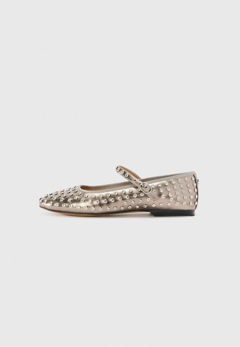 Beige metallinen tasapohjainen kenkä, jossa on terävä kärki ja hopeiset niitit. Yksi nauha jalkapöydän yli, jossa on solki. Tasapohja.