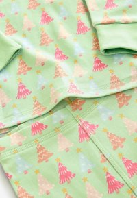 Tessuto verde chiaro con un motivo ripetuto di alberi di Natale colorati in rosa, blu e beige con accenti di stelle. Texture liscia.