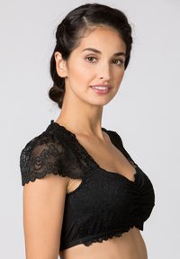 Schwarzer Spitzen-Bralette mit kurzen, gewellten Spitzenschultern, strukturierten Blumenmustern und einer gerafften Vorderseite. Darunter ein glatter schwarzer Körper.