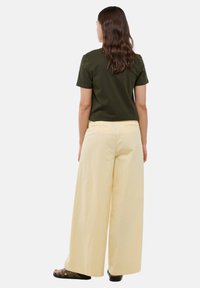 T-shirt olive vert à manches courtes, pantalon large taille haute jaune pâle, design minimaliste, texture lisse, et sandales noires à enfiler.