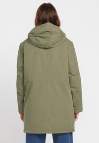 Parka vert olive avec capuche, présentant une coupe droite et des accents de couture. Tissu texturé, manches longues et poches latérales.