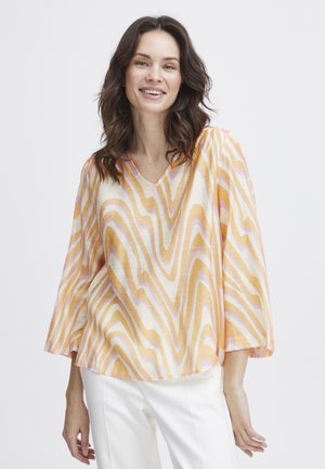 Chiffon bluse med V-udskæring, der har et bølget mønster i orange, gul og pink. Flared ærmer og en løs pasform for komfort. Hvide bukser bæres nedenunder.
