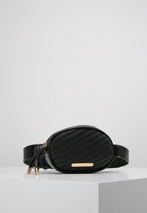 Marsupio ovale in pelle nera con cuciture diagonali, cerniere dorate e una piccola targhetta dorata del marchio sul davanti, esposto su una superficie bianca.