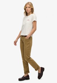 Camiseta de manga corta gris claro con texto rojo, combinada con chinos caqui enrollados y mocasines burdeos oscursos.