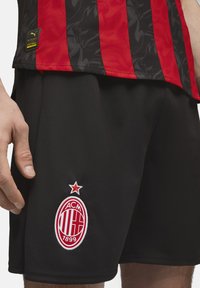 Rød- og sortstribet sportstrøje med sorte shorts. Har en tekstureret finish og et broderet rødt og hvidt AC Milan-logo med en stjerne.