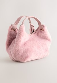 Roosa pehme käekott nahksangadega, pehme tekstuur, ümar kuju ja minimalistlik disain. Sangade lähedal on kuldse tooni metalldetailid.