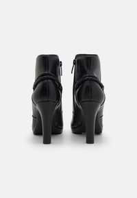 Zwarte leren enkellaarsjes met hoge hakken, voorzien van een gevlochten detail en zijritsen. Gladde textuur en gestroomlijnd ontwerp.