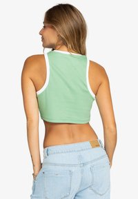 Top corto verde con ribete blanco; textura acanalada. Llevado con jeans de tiro alto en azul claro, mostrando una vista trasera.