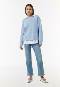 Lichtblauwe sweatshirt met een kraag, geborduurd met "Mind Your Soul", gecombineerd met lichtblauwe jeans en metallic zilveren platte schoenen.