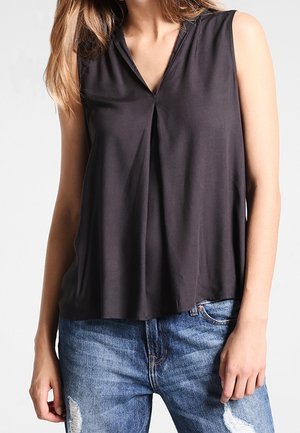 Mouwloos donkergrijs topje met een V-hals en plooidetail. Gemaakt van zacht materiaal, met een relaxte pasvorm en gecombineerd met blauwe spijkerbroek met slijtageplekken.
