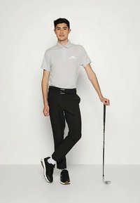 Sivá polokošela s krátkymi rukávmi, čierne nohavice a čierne tenisky. Póza v stoji s golfovou palicou v ruke. Jednoduchý dizajn, minimálne označenie.