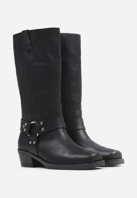 Botas negras de piel hasta la rodilla, con puntera redonda, tacón bajo y una correa con un detalle decorativo metálico. Textura suave y diseño minimalista.