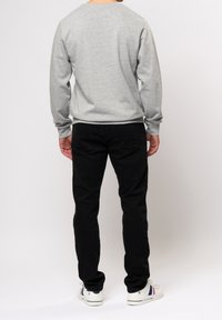 Felpa grigia con maniche lunghe e colletto rotondo, abbinata a pantaloni neri e sneakers bianche con dettagli colorati.