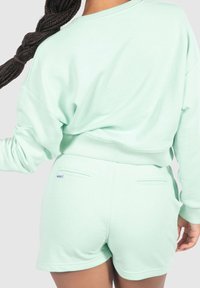 Felpa verde menta con maniche lunghe e vestibilità morbida, abbinata a pantaloni corti verde menta coordinati con tasche posteriori discrete.