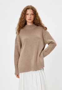 Maglione beige a maglia con colletto alto e spalle scese. Presenta polsini a coste e un orlo laterale aperto, realizzato in un materiale morbido.