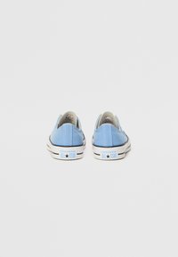 Világoskék vászon slip-on cipők lekerekített orral, fehér gumis orrvéggel, fekete csíkkal és "CONVERSE ALL STAR" logóval a sarkon.