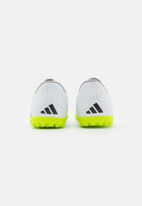 Scarpe da calcio bianche con suola verde lime, caratterizzate da accenti neri e una texture liscia. Progettate per superfici in erba sintetica.