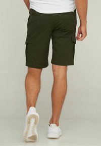 Shorts cargo vert olive à coupe droite, avec deux poches latérales et un ourlet juste au-dessus du genou. Portés avec des baskets blanches.