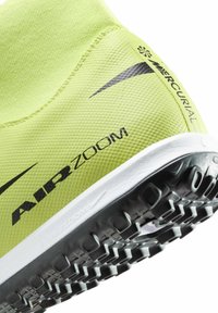 Lys gul atletiksko med en tekstureret overdel, sorte accenter og en fleksibel gummisål med små, forhøjede nubringer for bedre greb.