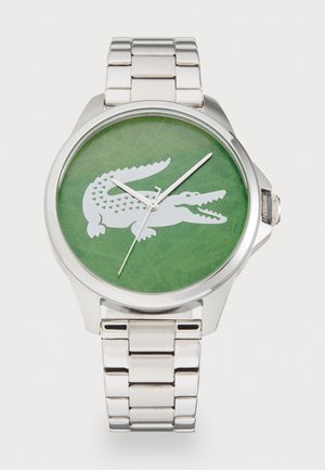 Montre en métal argenté avec un cadran circulaire vert arborant un design de crocodile blanc. Aiguilles fines en argent et bracelet à maillons.