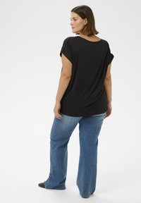 Tricou negru, cu croială relaxată, cu mâneci răsucite, asortat cu blugi largi de un albastru deschis. Țesătură netedă, vedere din spate cu tiv rotunjit.