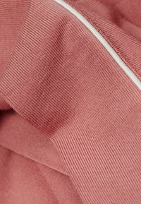 Texturerad bomullstyg i mjuk rosafärg, med en ribbad design och kontrasterande vit trim längs sömmen.