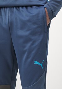 Pantaloni atletici blu navy realizzati in tessuto testurizzato con cintura elasticizzata, dotati di tasche laterali e un logo azzurro chiaro sulla coscia.