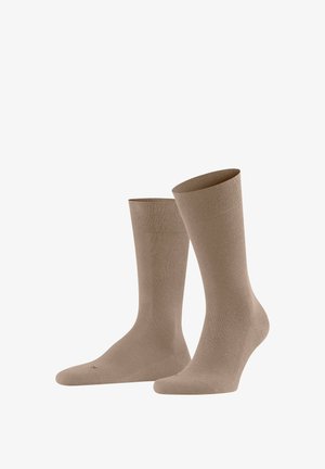 Paar schlichte beige Socken mittlerer Länge, aufrecht präsentiert, wobei ein Socken leicht hinter dem anderen auf weißem Hintergrund steht.