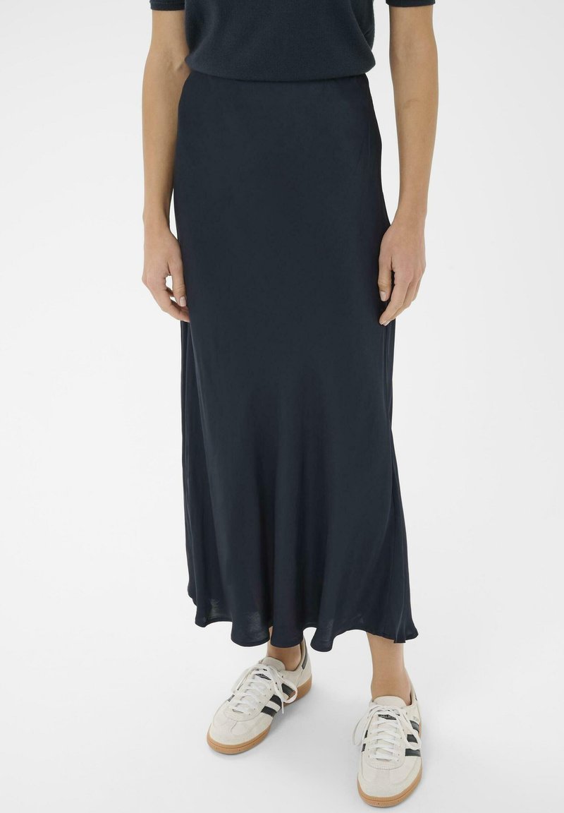 Melnā, plūstošā maksi svārku izgatavota no viegla auduma ar gludu tekstūru, saskaņota ar baltām kedām, kurām ir melnas svītras.