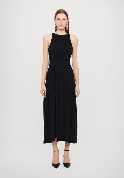 Vestido maxi negro con un corpiño ajustado y detalles fruncidos, que presenta una falda fluida. Accesorios con pendientes geométricos y tacones puntiagudos.