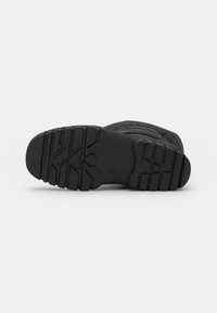 Bota de invierno negra tumbada de lado, mostrando su suela de goma gruesa con patrones de tread profundos para un mejor agarre.
