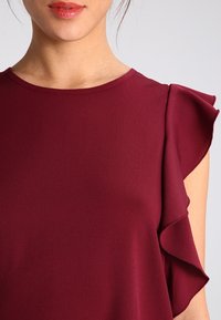 Bourgogne bluse med korte flæsermer, glat tekstur, rund halsudskæring og blødt fald. Ingen synlige mønstre eller hardware.