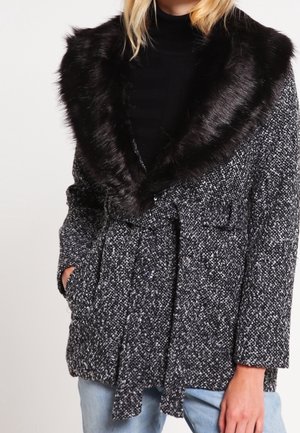 Abrigo de manchas en blanco y negro con un gran collar de piel sintética, que presenta una cintura con cinturón, dos bolsillos frontales y un diseño de tejido texturizado.