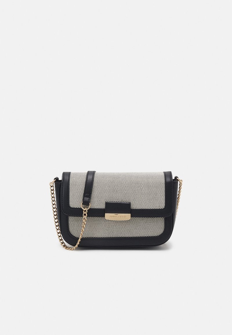 Borsa a mano in rete bianco e nero con forma strutturata, tracolla a catena dorata e chiusura magnetica rettangolare. Presenta una placca con logo sulla parte frontale.