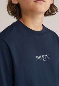 Námořnická modrá bavlněná tričko s kulatým výstřihem a bílou grafikou "BLUE RIDGE" s obrysy hor na přední straně.