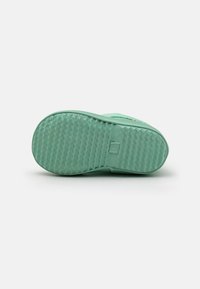 Semelle de chaussure en caoutchouc verte avec un motif texturé, des bords lisses et un détail de marque. Forme arrondie conçue pour la flexibilité et l'adhérence.