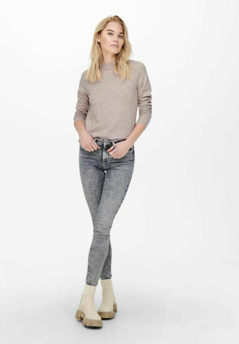 Lichtbeige gebreide trui, grijze verouderde jeans en crèmekleurige enkelboots met dikke zolen. Eenvoudig ontwerp en aansluitende silhouet.
