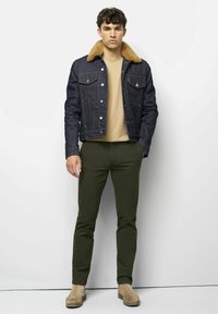 Denim jacket met een tan nepbont kraag, blauwe denim en voorzakken, gecombineerd met olijfgroene broek en beige enkellaarzen.