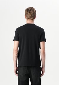 T-shirt en coton noir, à manches courtes, col rond, coupe régulière, texture lisse, design épuré, associé à un jean en denim foncé.
