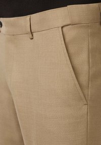 Beżowe spodnie z teksturowanej tkaniny, z płaskim przodem, bocznymi kieszeniami i gładkim pasem, zaprojektowane dla dopasowanego kroju.