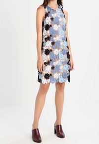 Ärml dress med blommig spets i blått, vitt och svart. Spretig nederkant och en avslappnad passform. Matchas med vinröda öppna tofflor.