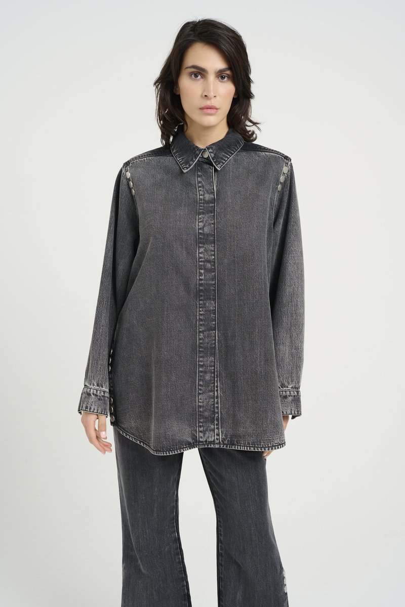 Černá oversized košile z denimu s límečkem, zapínáním na knoflíky a detailním prošíváním. Dlouhé rukávy mají knoflíkové ozdoby na švu.