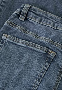 Jeans en denim bleu moyen avec une texture lisse, présentant un design de poche standard et des coutures contrastantes en orange.